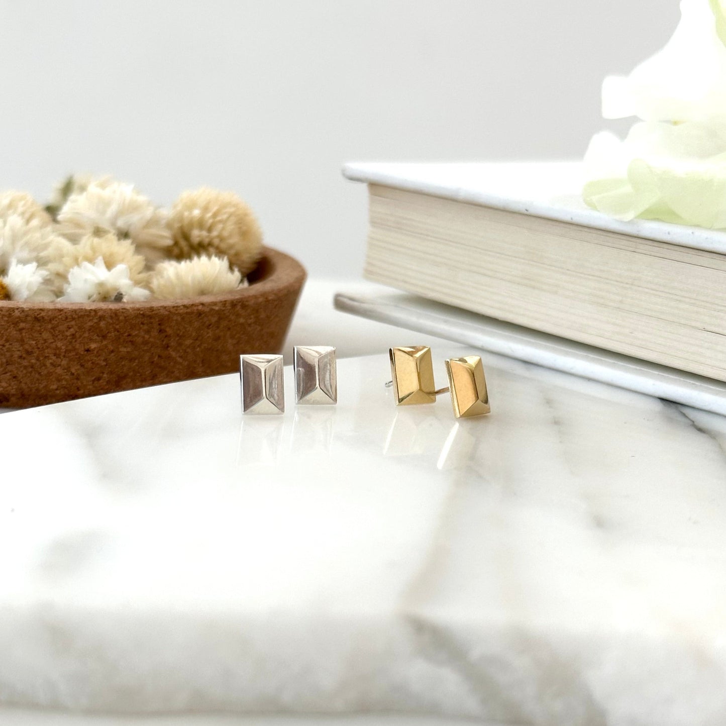 a pair of gold and silver faceted stud earrings displayed on a piece of marble with a textured white background