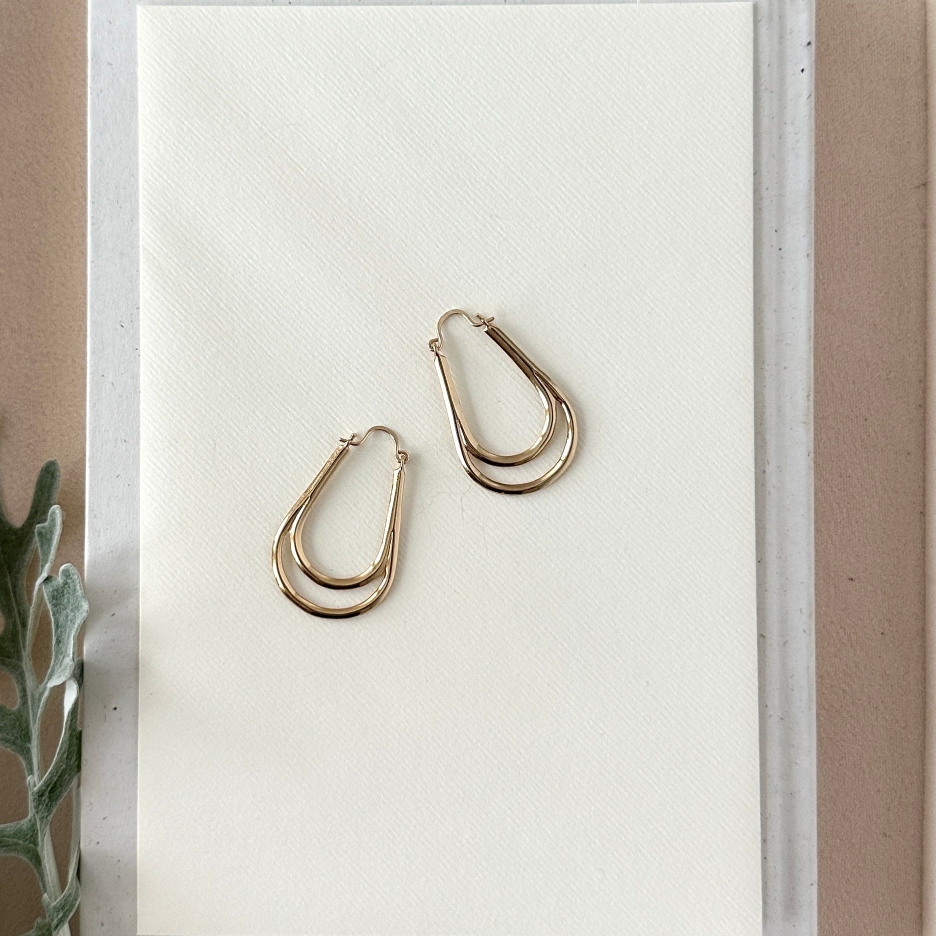 Gold hoop earrings on a white card with a minimal background