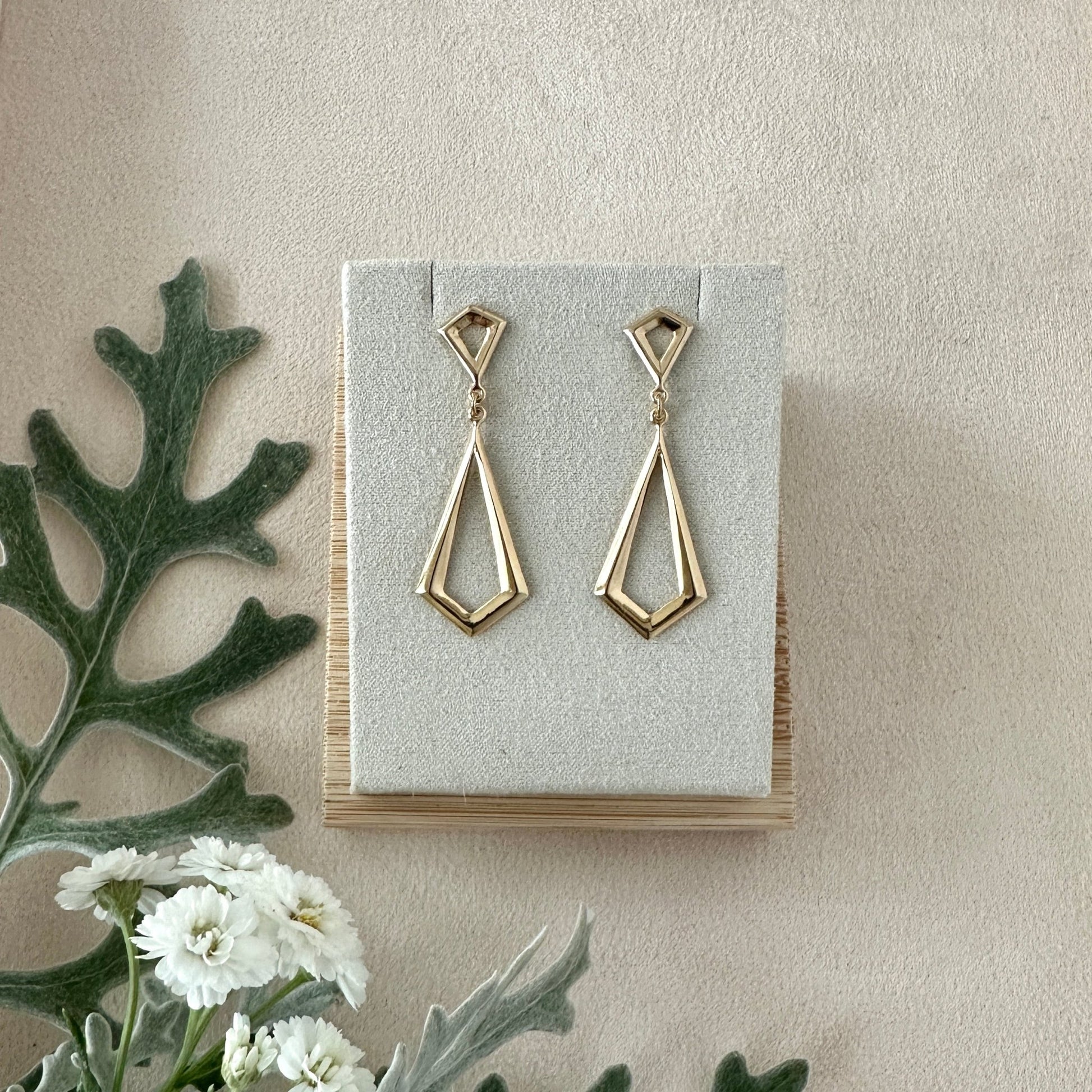 Gold geometric drop earrings on a display card with a natural background