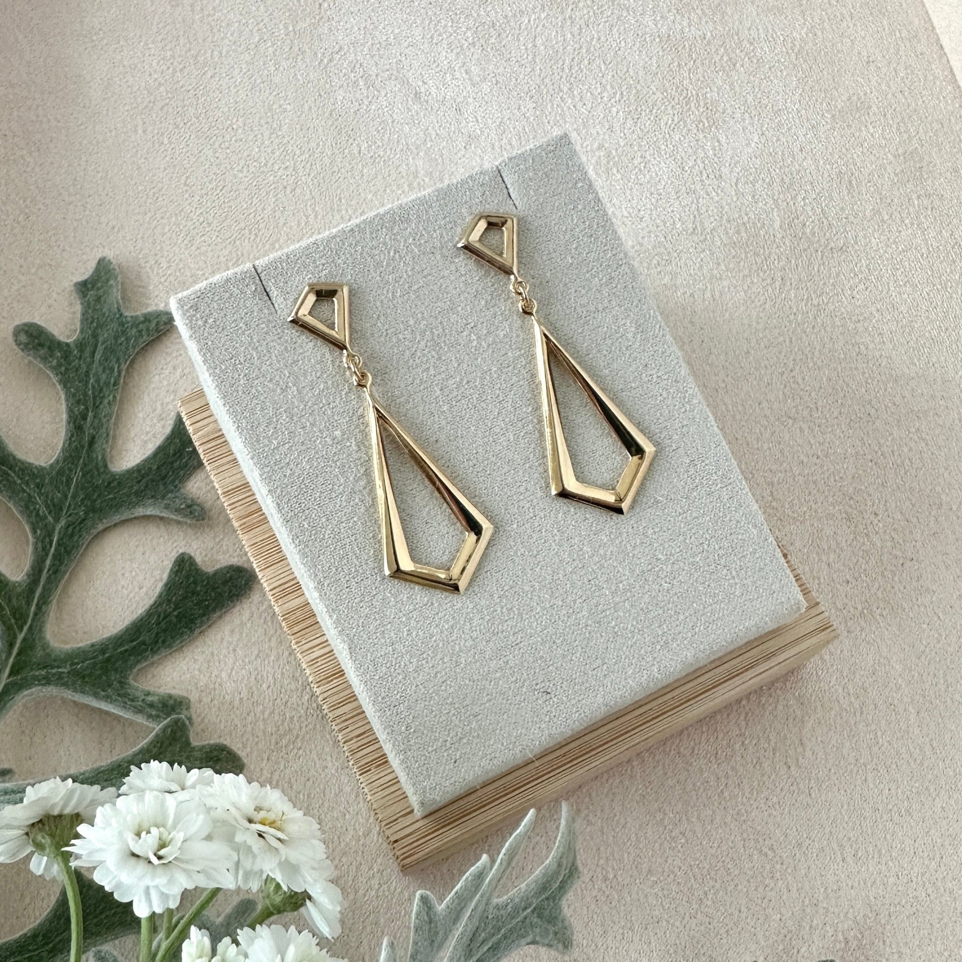 Gold geometric drop earrings on a display card with a light background