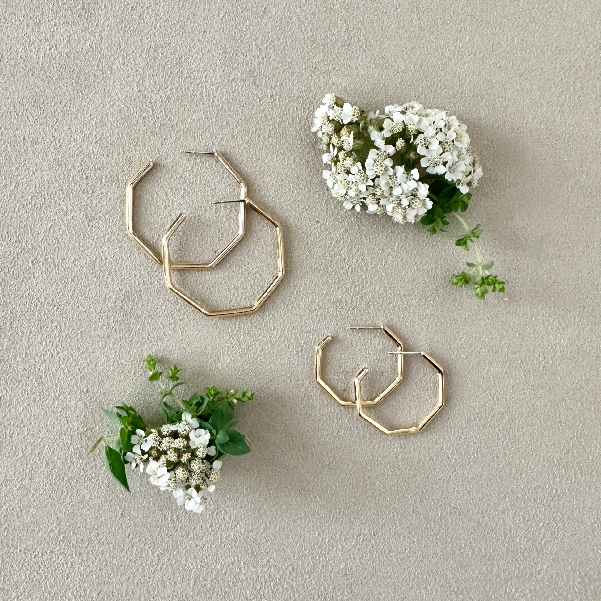 Gold hoop earrings with small white flowers and green leaves on a light gray background