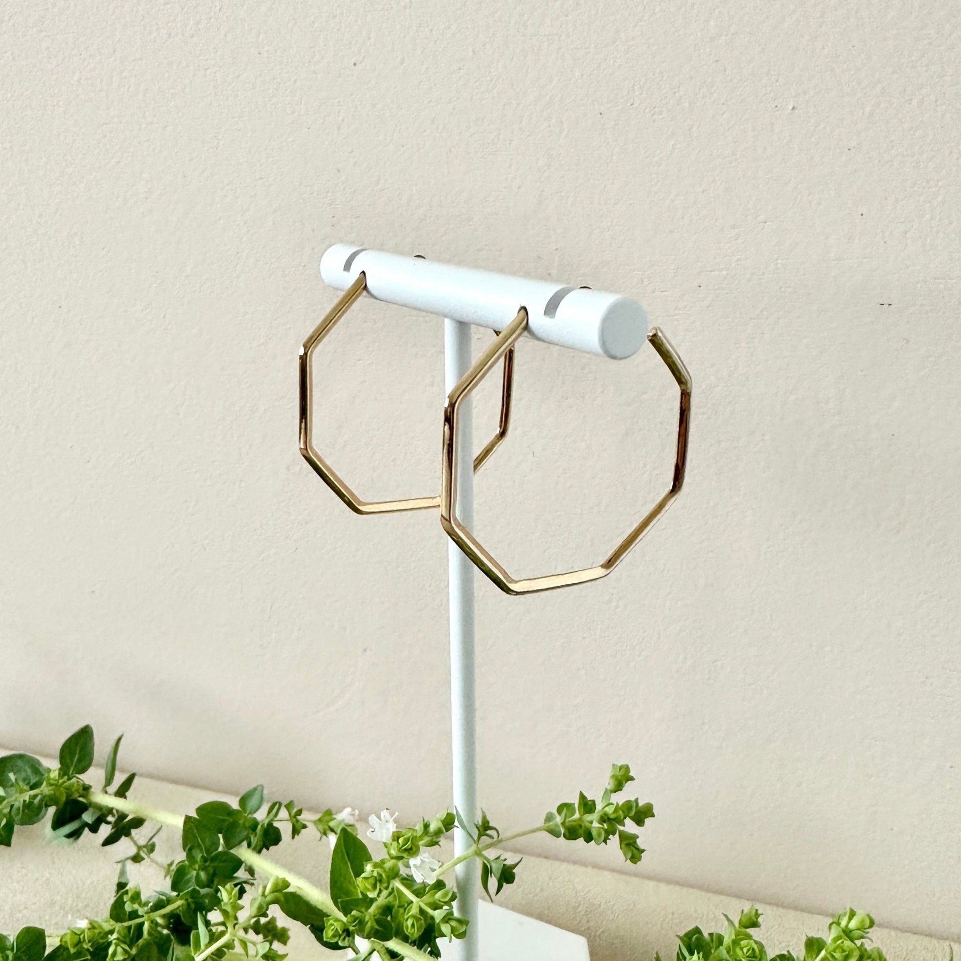 Gold hoop earrings on a white stand with a neutral background