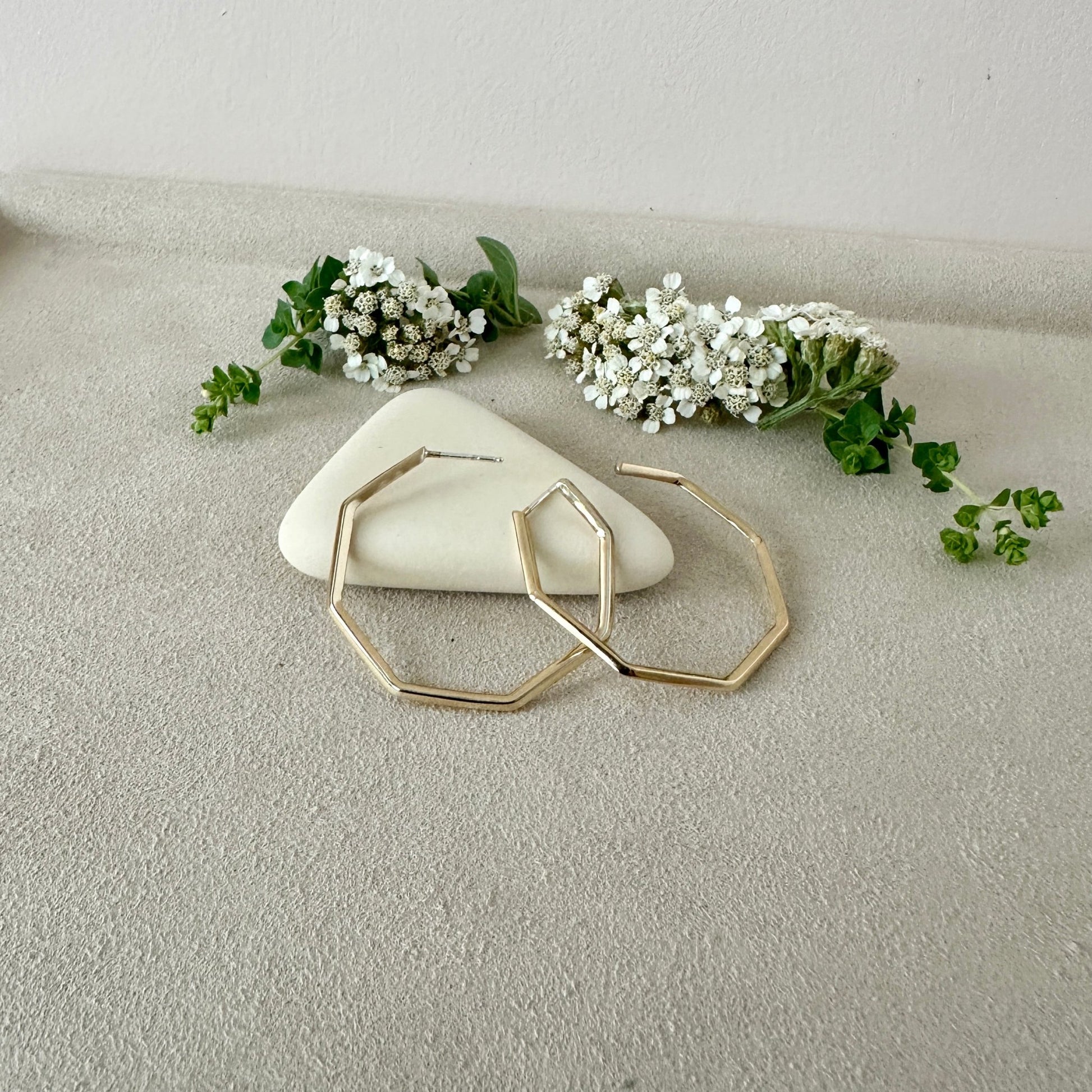 Gold hoop earrings on a light surface with small white flowers and green leaves.