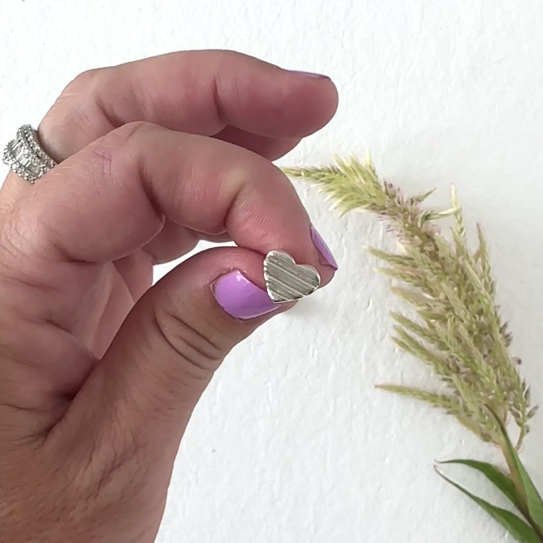 Hand modeling a silver heart stud earring on a neutral background