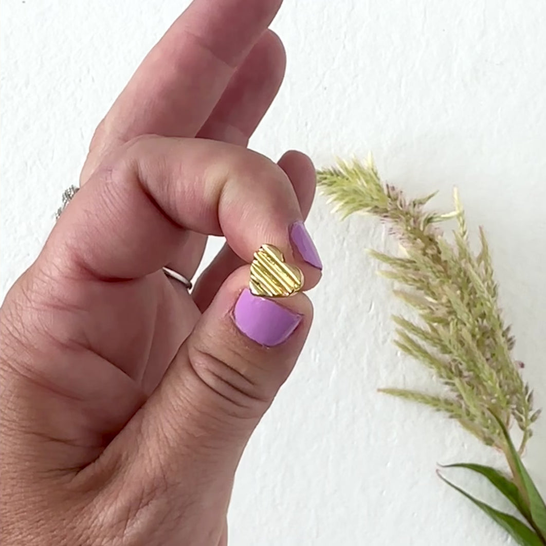 hand modeling a gold heart stud earring with neutral background