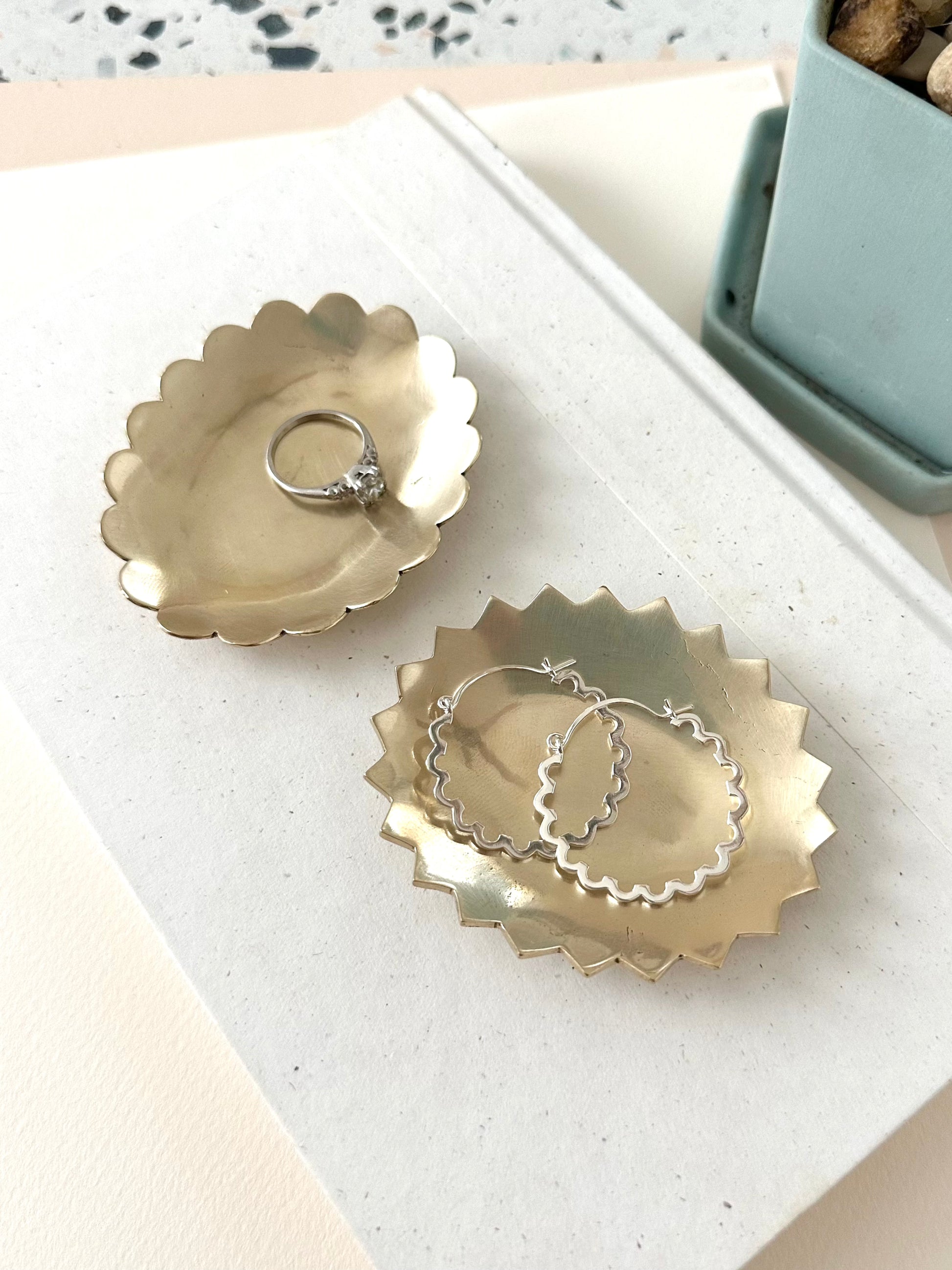 Sarah Cecelia Brass Ring Dishes with a diamond ring and silver hoop earrings on a neutral background with sage green pot.
