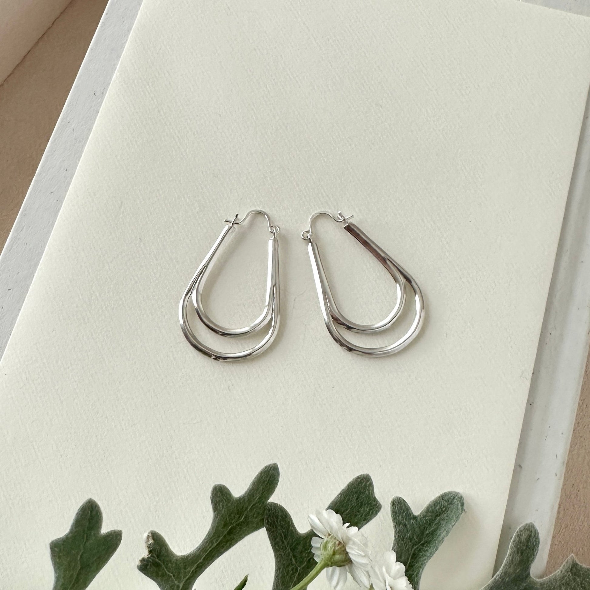 Silver hoop earrings on a white surface with greenery