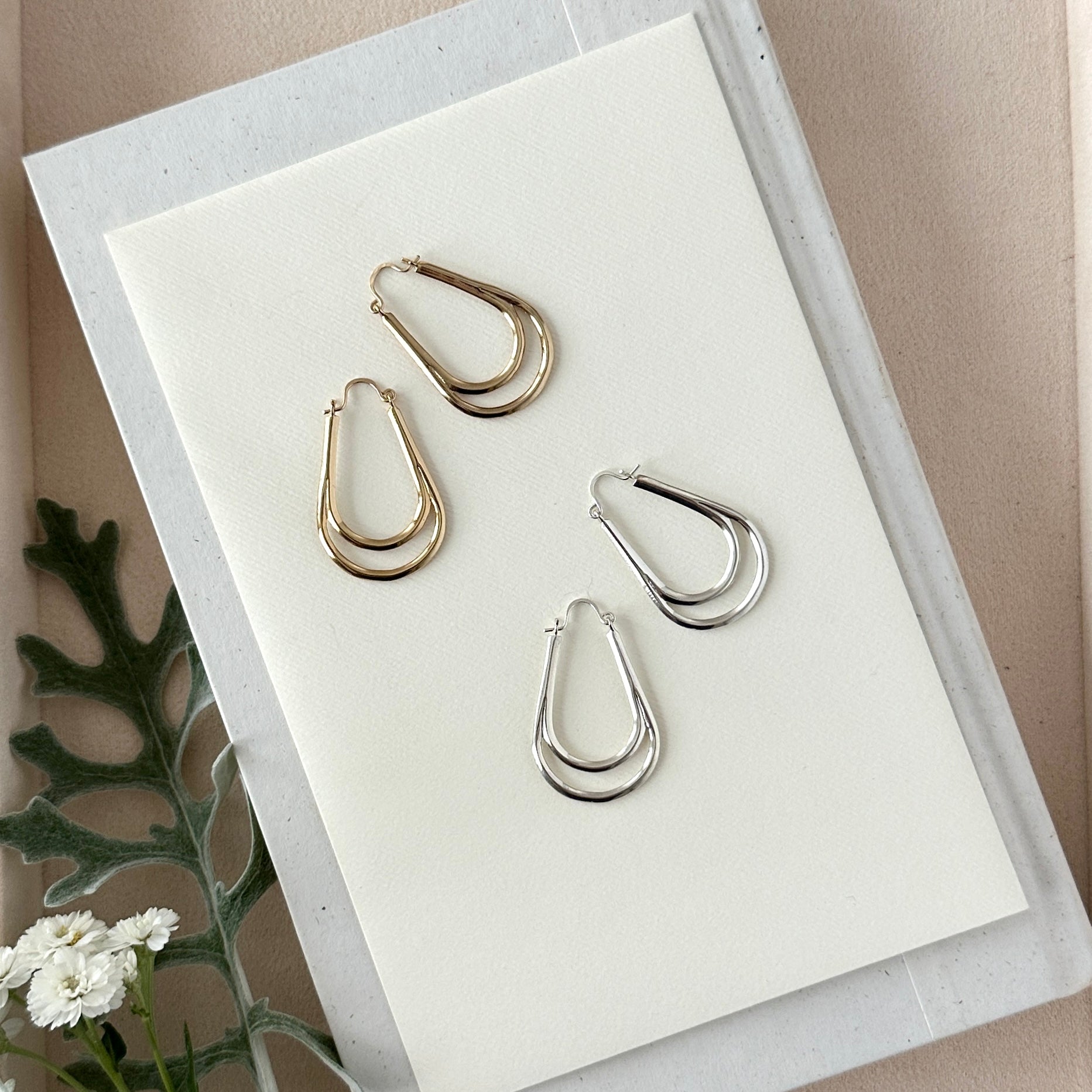 Set of gold and silver hoop earrings on a white card with a beige background