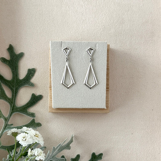Silver drop earrings on a display card with a light background and greenery.