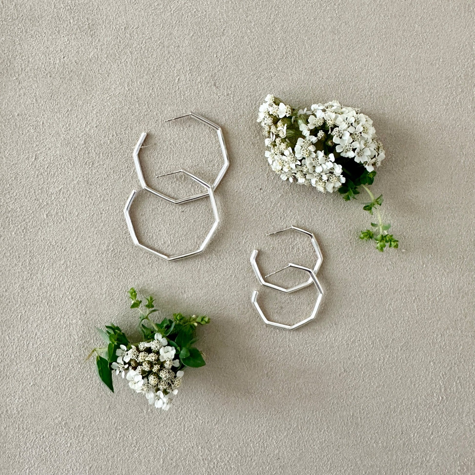Silver geometric earrings with small white flowers on a beige background