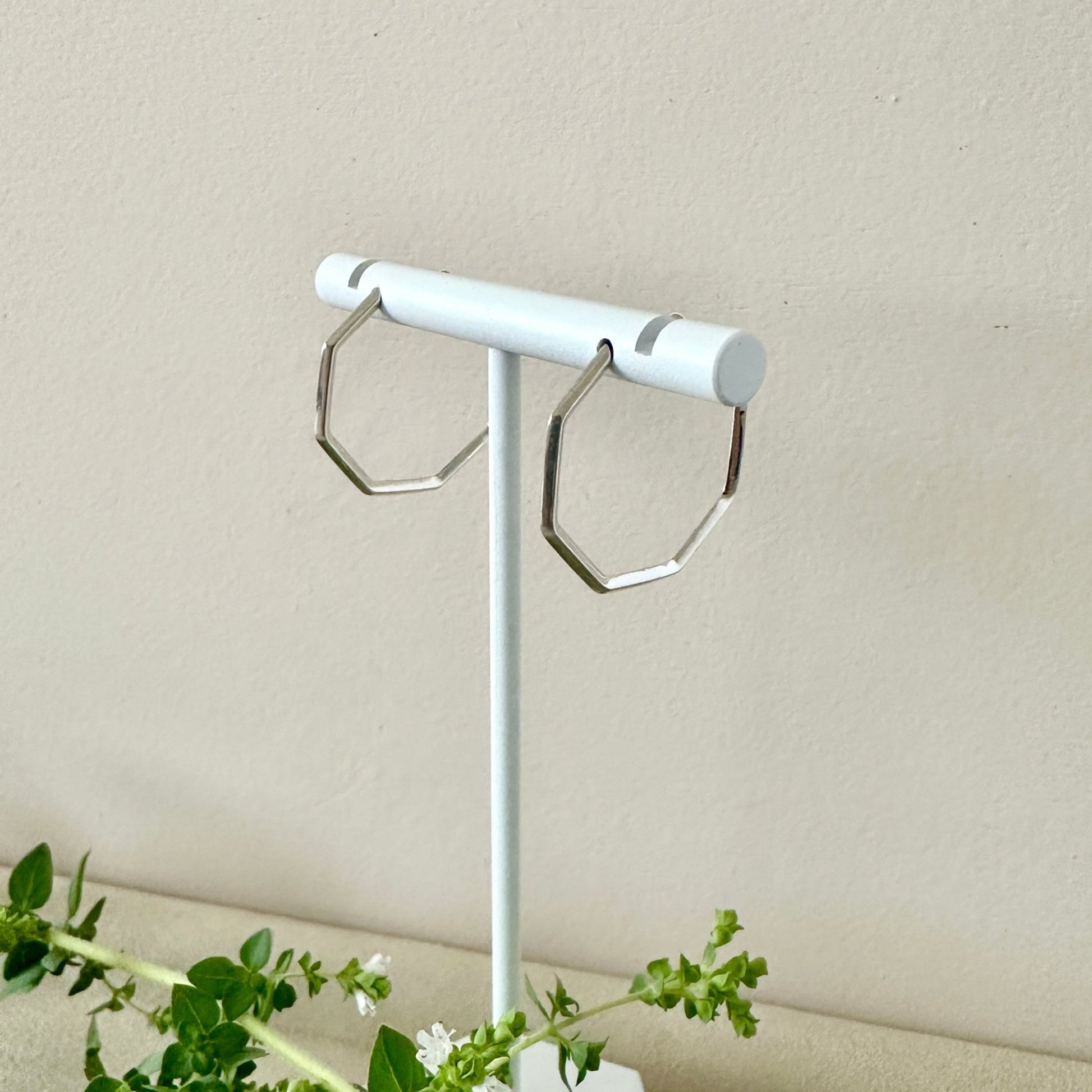 SIlver hexagonal hoops on a white stand with neutral background