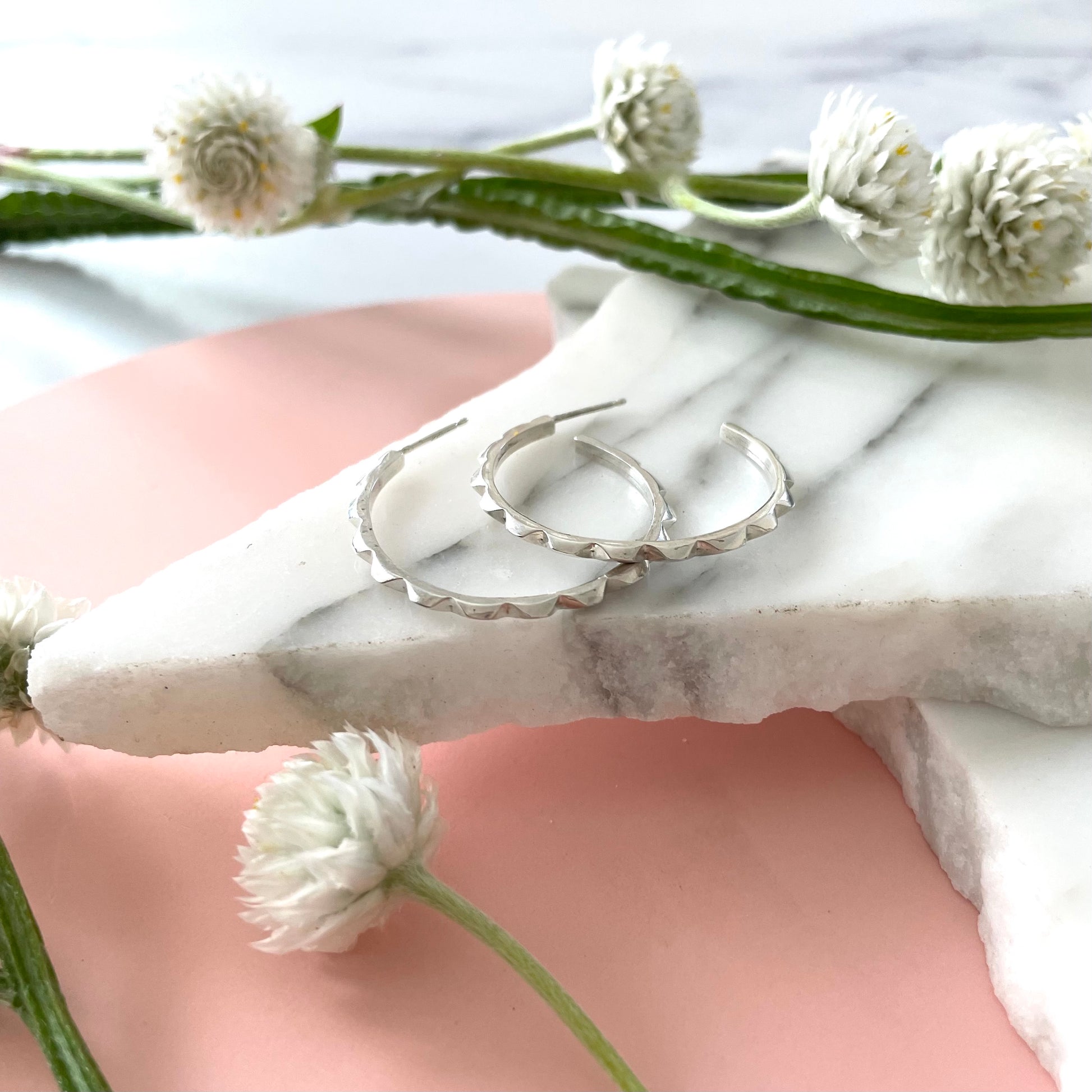 Handmade sterling silver hoop earrings on a marble displayed with a pink background and fresh flowers