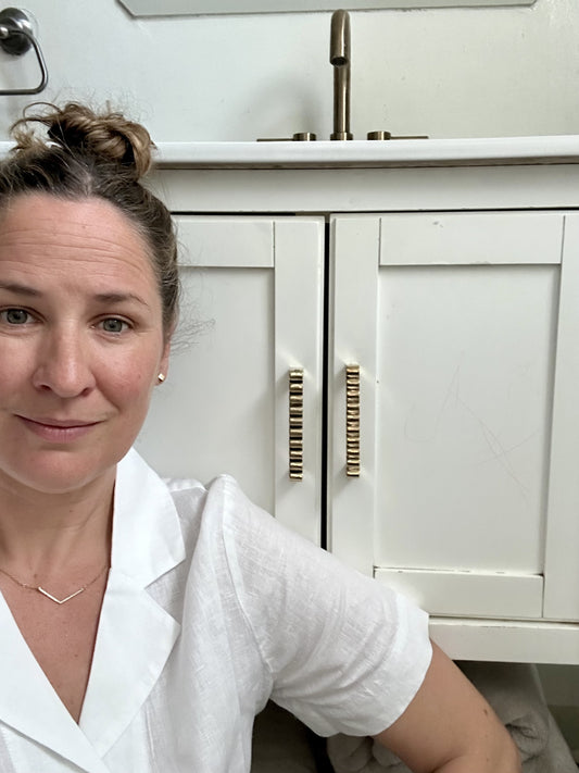 The designer Sarah Cecelia in front of a white bathroom cabinet with handmade brass handles