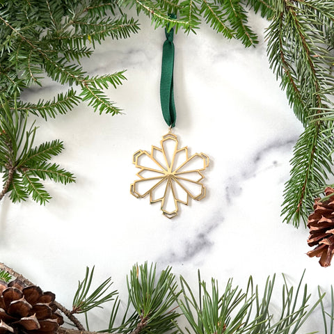 A handmade Brass Snowflake displayed on a marble background surrounded by greenery and pinecones