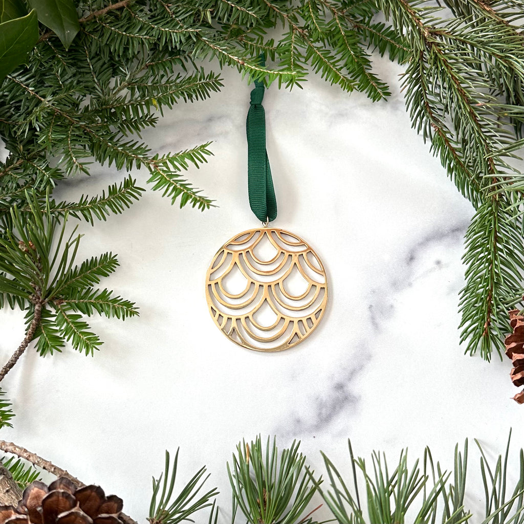 A brass deco christmas ornament on a marble background surrounded by greenery with pinecones