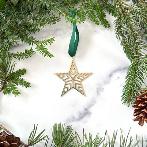 A handmade brass star christmas ornament on a marble background surrounded by greenery and pinecones