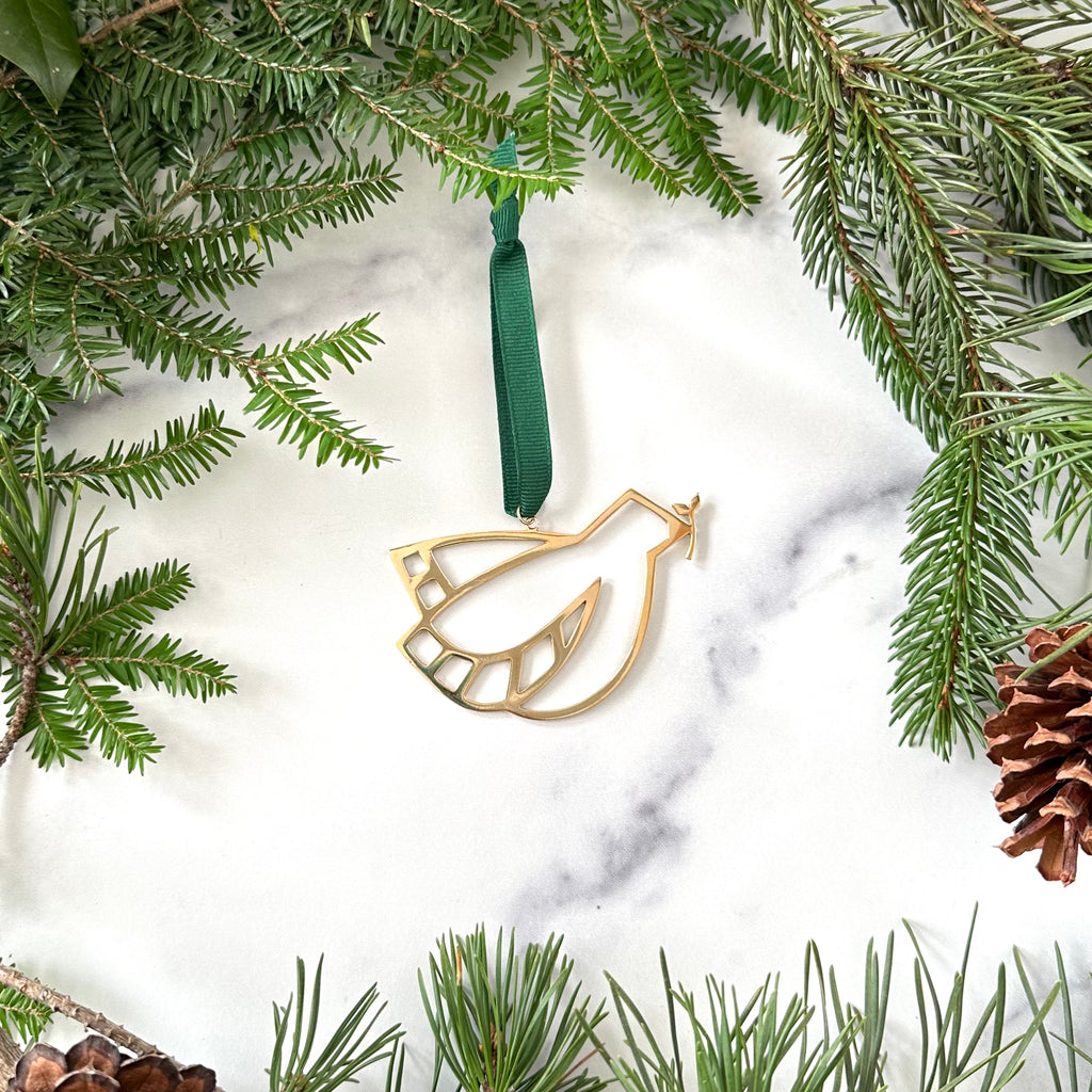A handmade brass peace dove ornament on a marble background surrounded by greenery and pinecones 