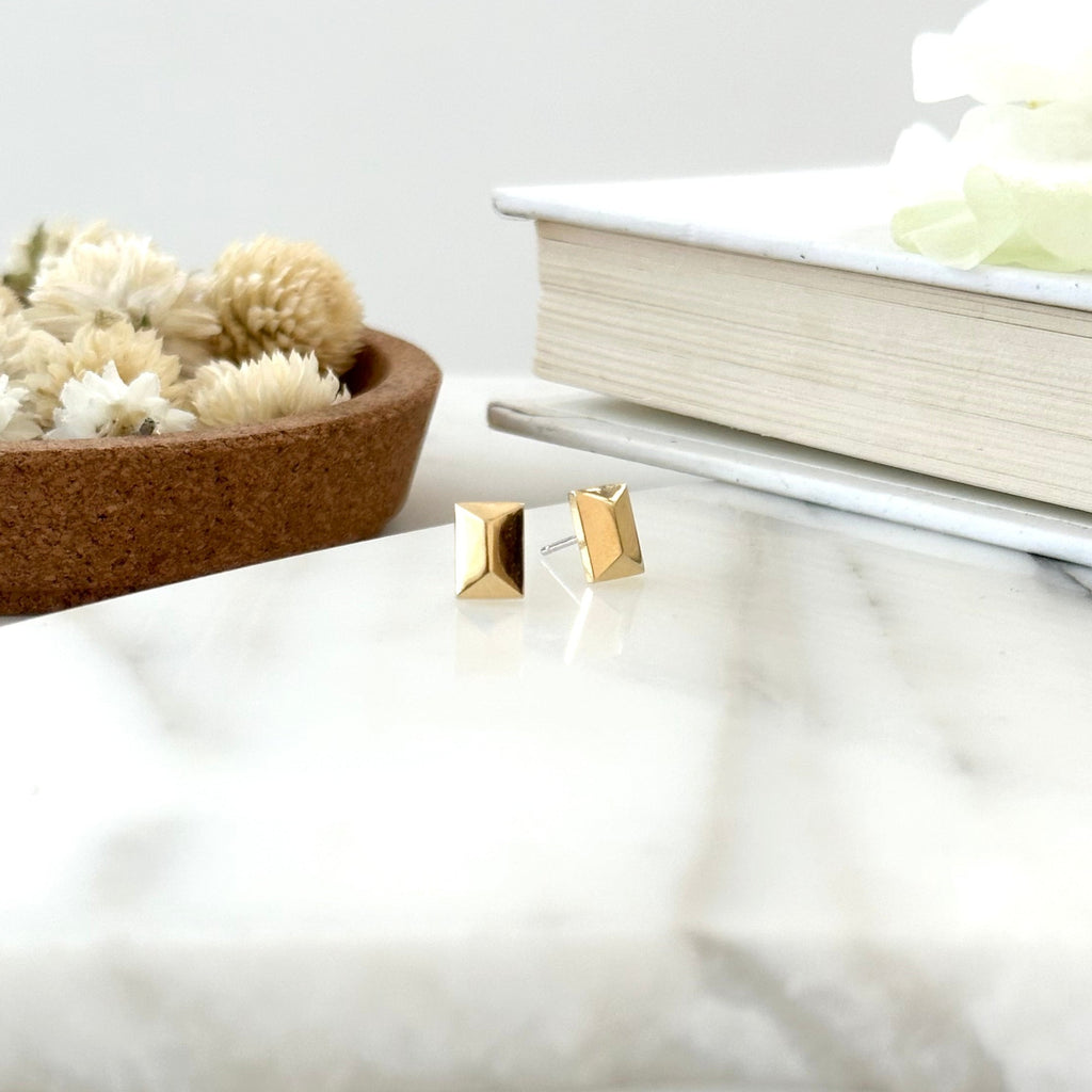 a pair of gold faceted stud earrings displayed on a piece of marble with a textured white background