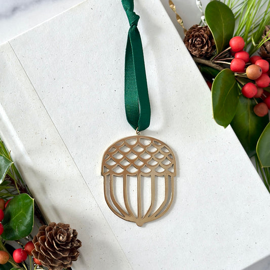 Decorative acorn-shaped ornament with a green ribbon on a white surface with foliage.
