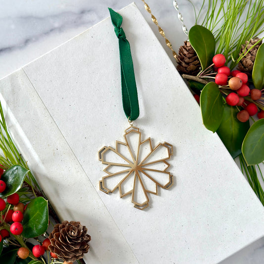 Gold snowflake ornament with green ribbon on a white surface with festive decorations.
