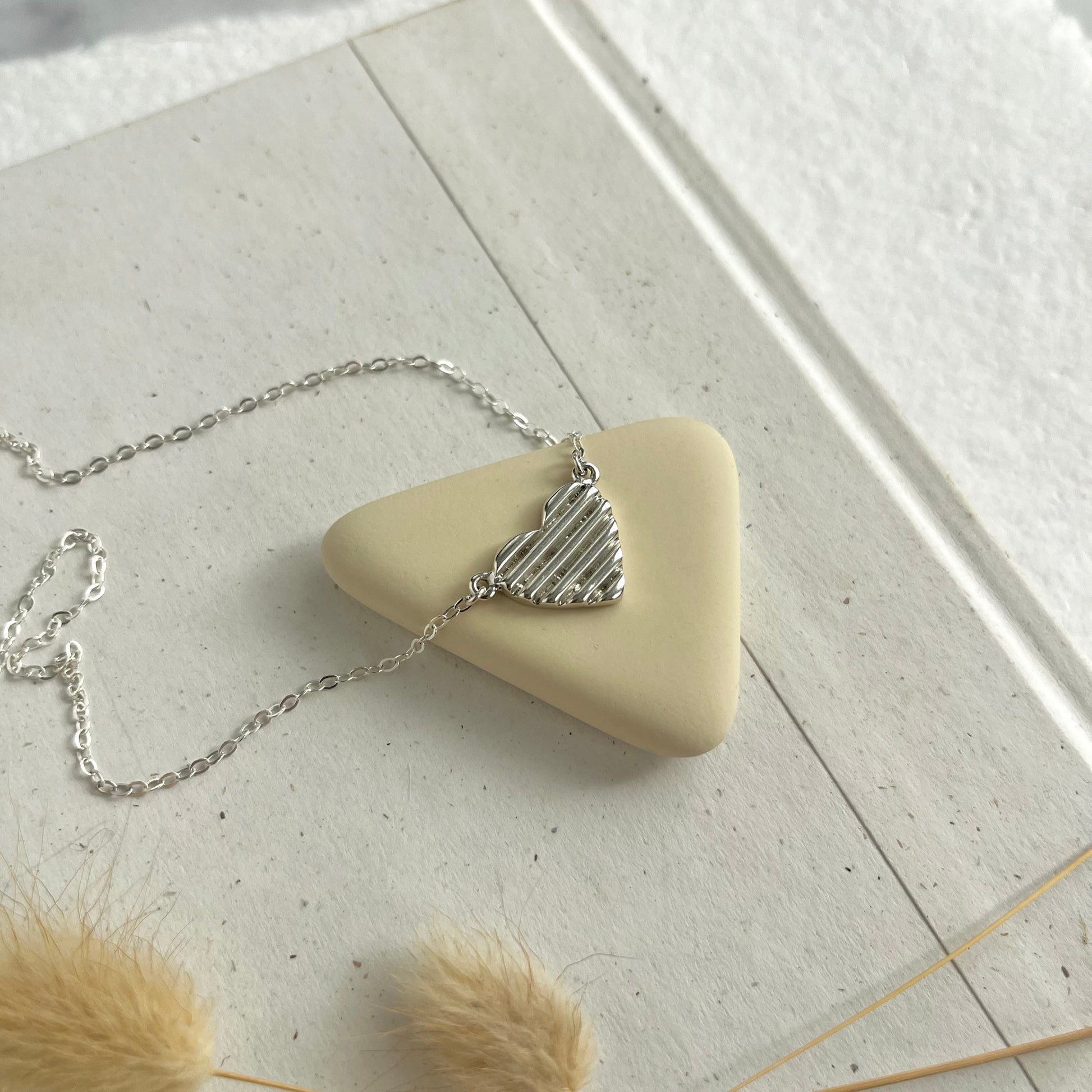 A sterling silver hand carved heart necklace on a neutral background. 