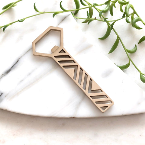 A geometric brass bottle opener on a marble slab with greenery