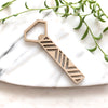 A geometric brass bottle opener on a marble slab with greenery