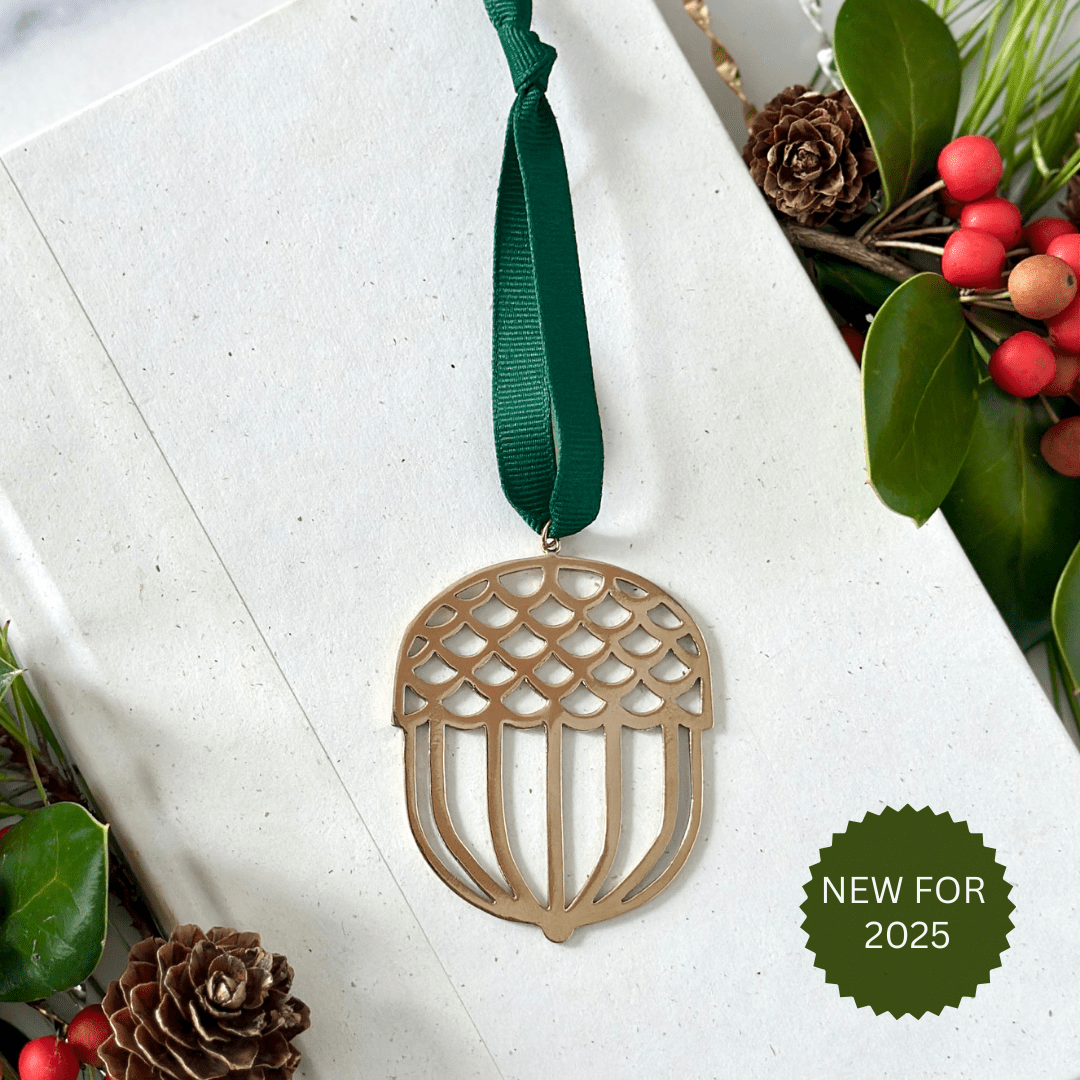 Decorative acorn ornament with green ribbon on a white surface with Christmas elements.