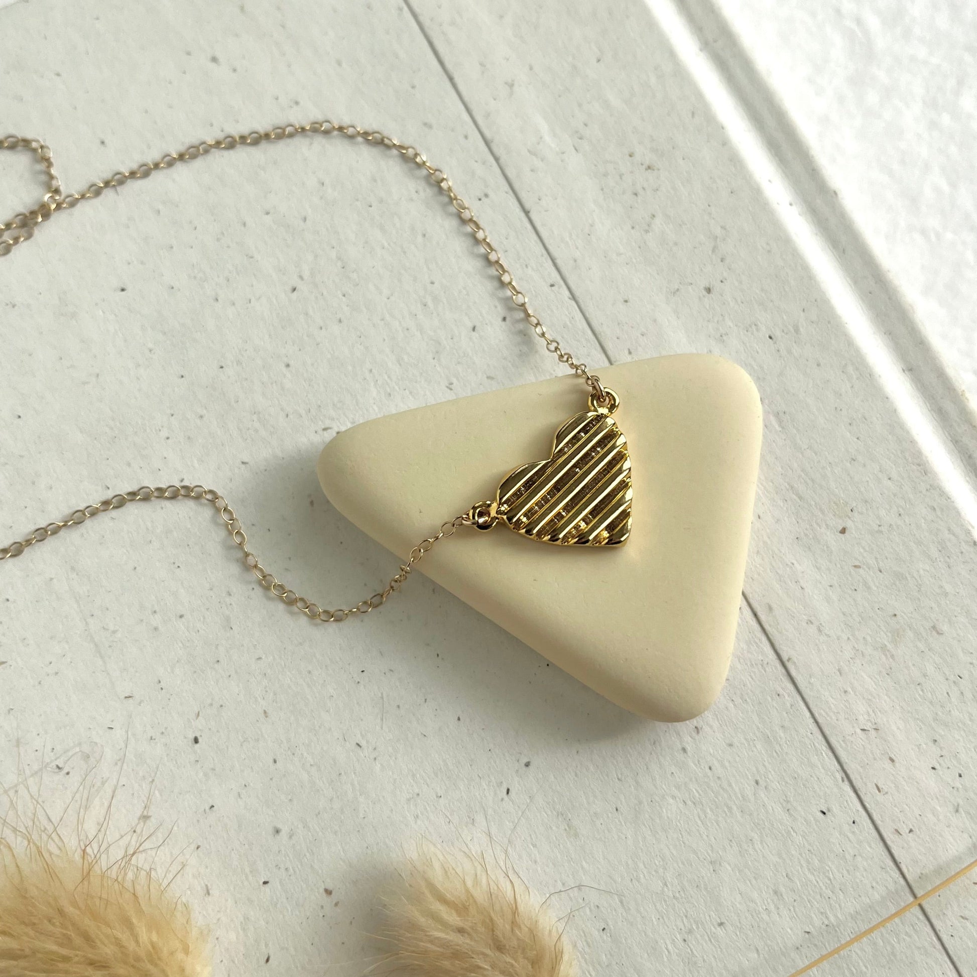 detail shot of the scala heart necklace in gold by sarah cecelia on a neutral background