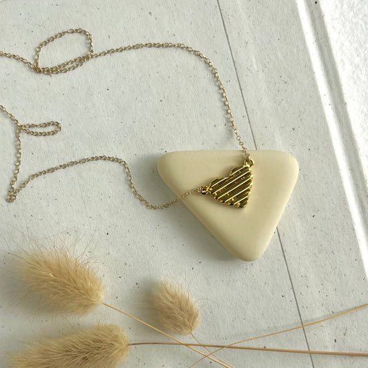 A hand carved gold heart necklace by sarah cecelia on a neutral background 