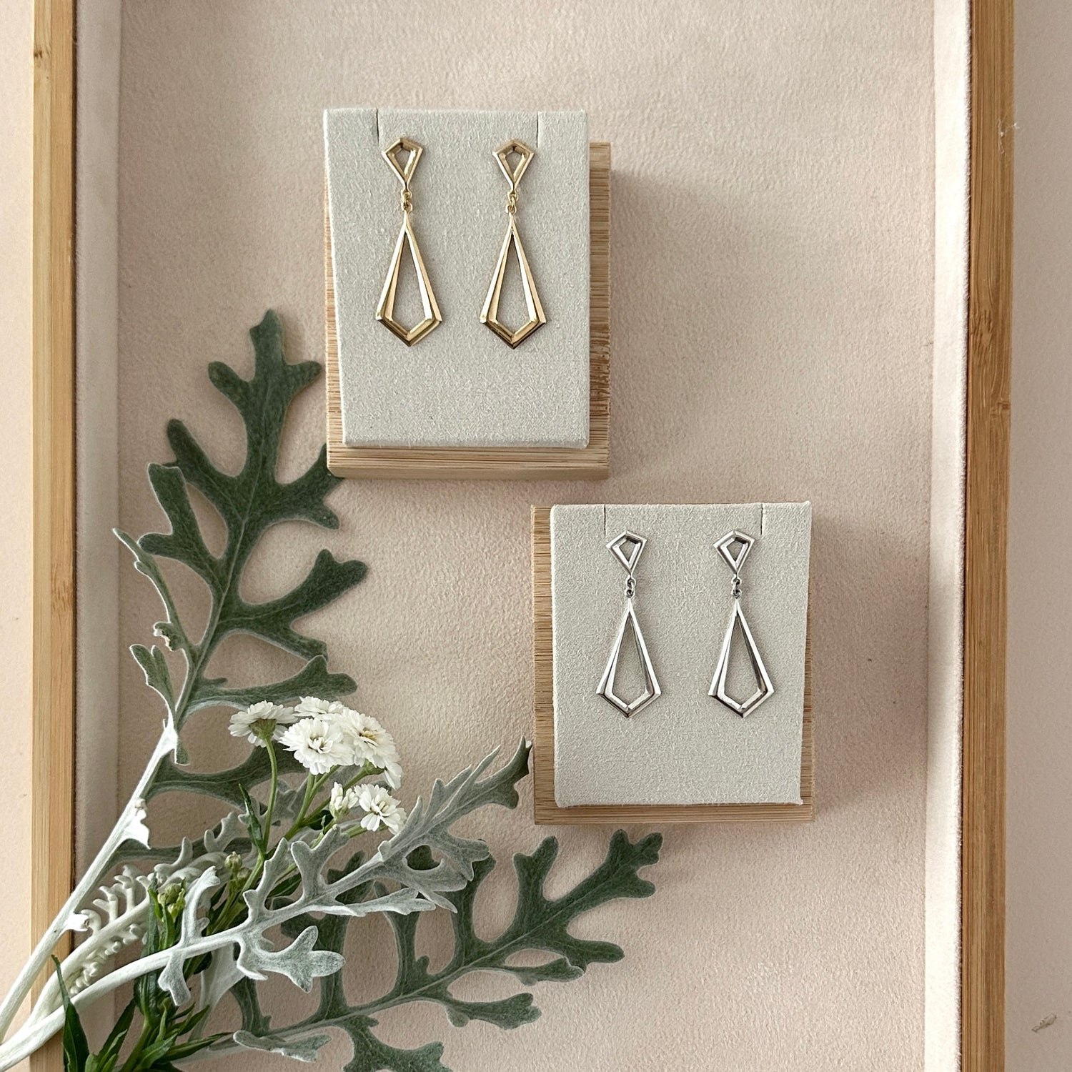 Pair of gold and silver geometric drop earrings on display with greenery.