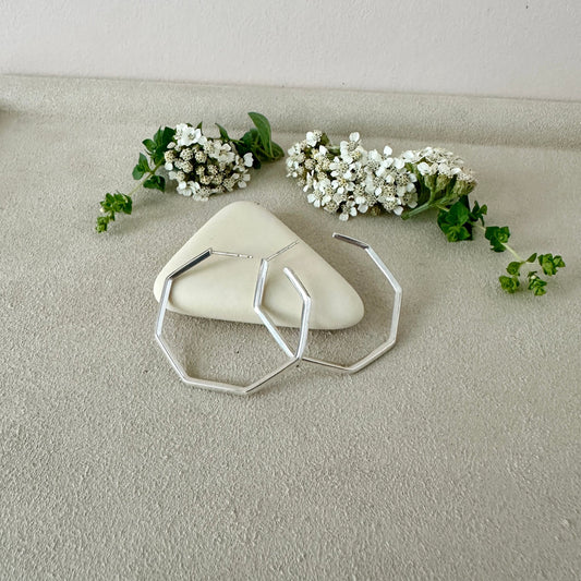 silver geometric hoops on a textured surface with small white flowers and green leaves.