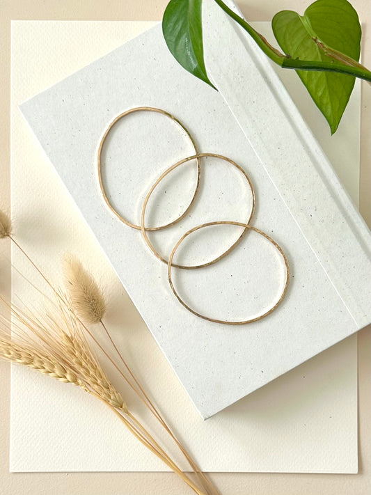 three handmade gold fill bangle bracelets displayed on a book with dried grass and greenery