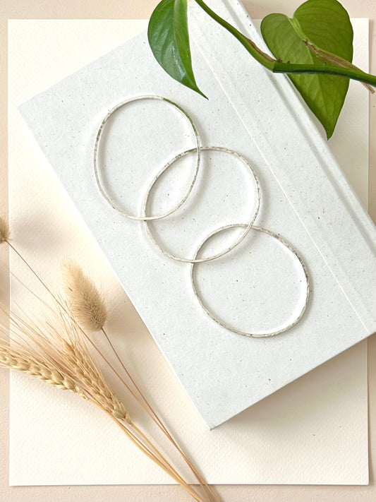 Three sterling silver bracelets displayed on a book with dried grasses and greenery