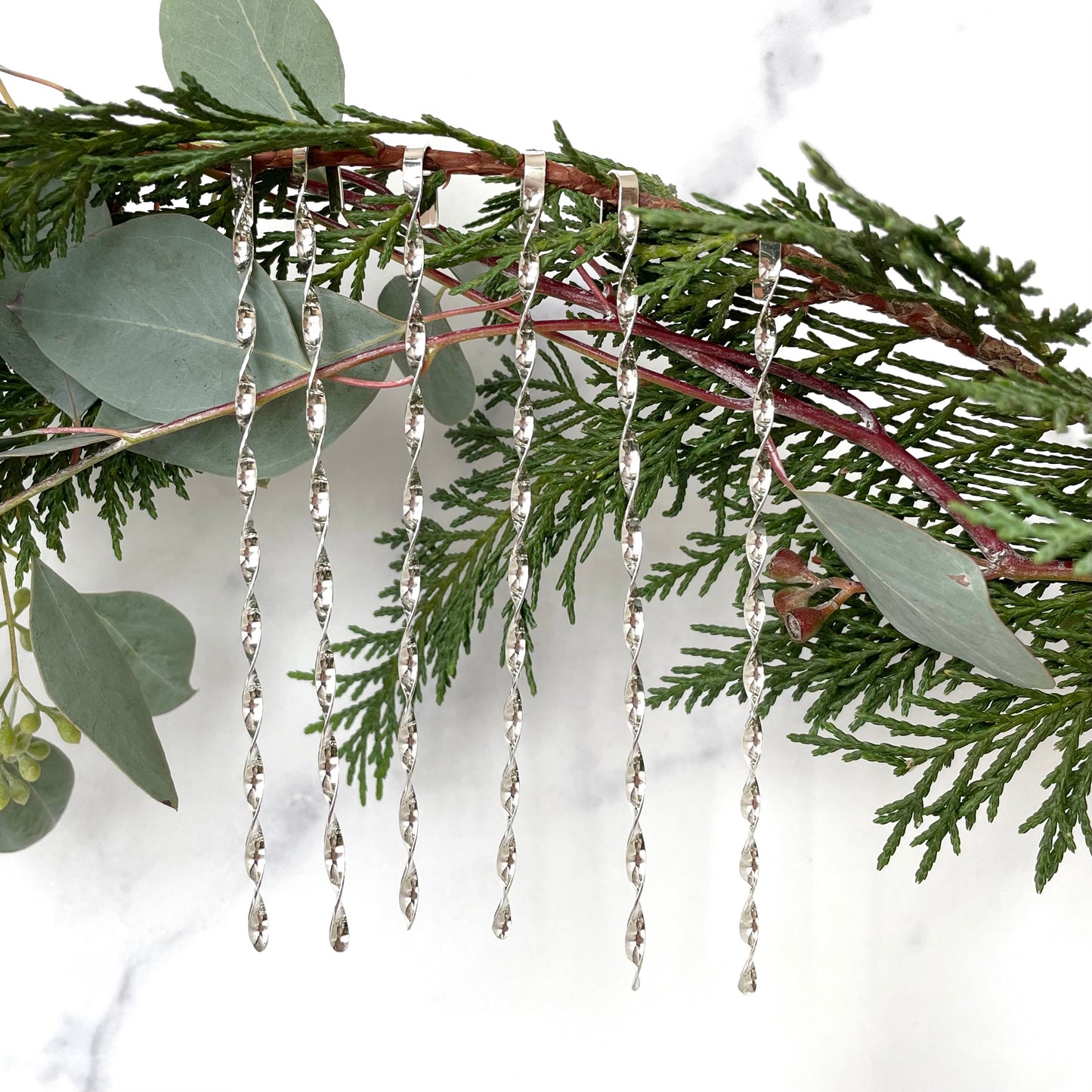 six sterling silver christmas tree ornaments displayed on greenery with a white background 