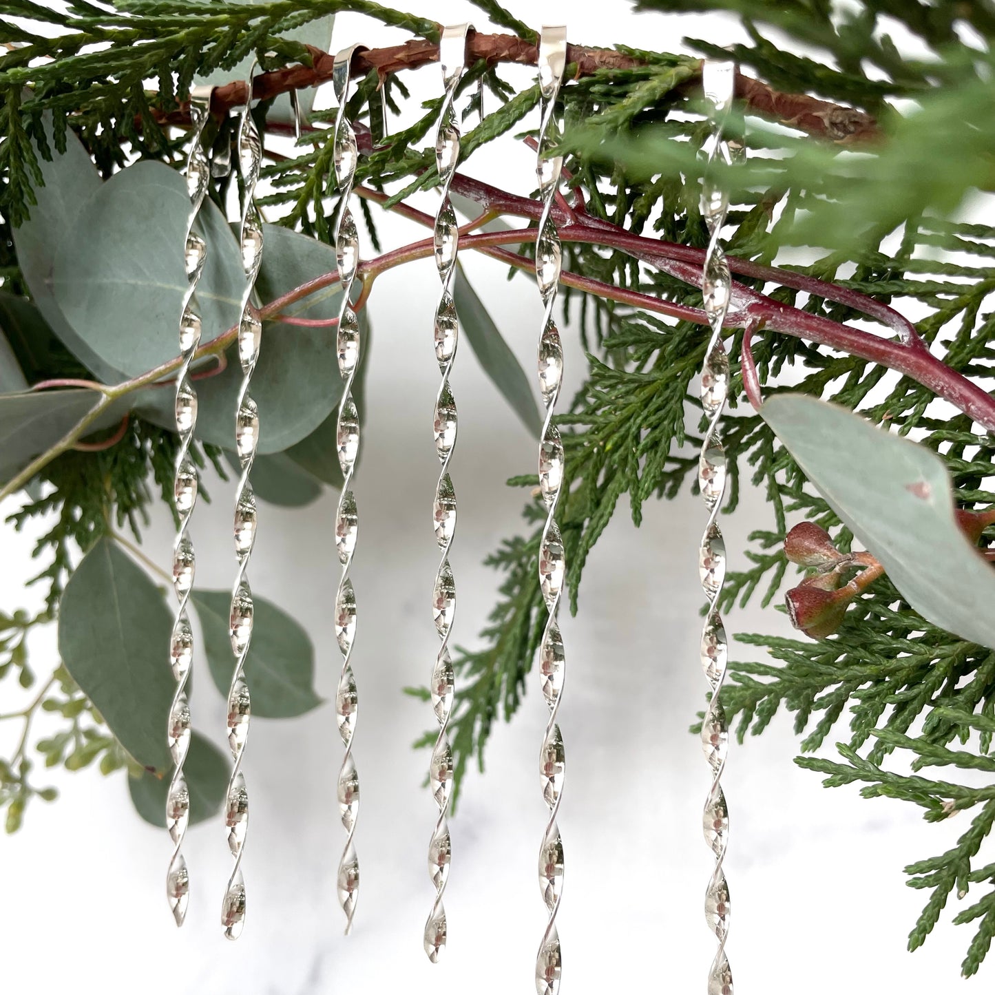 six sterling silver christmas tree ornaments displayed on greenery with a white background