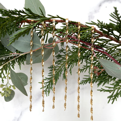 six gold christmas tree ornaments displayed on greenery with a white background