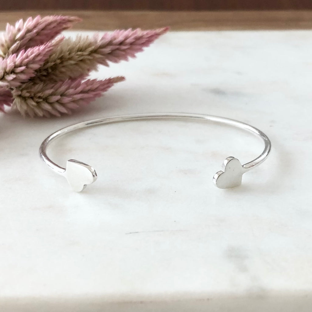 Sterling Silver cuff heart bracelet displayed on marble with a flower in the background.