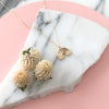 Gold rainbow necklace displayed on a piece of marble with a pink background and dried flowers