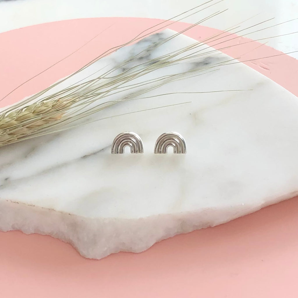 a pair of sterling silver rainbow stud earrings displayed on a piece of marble with a pink background