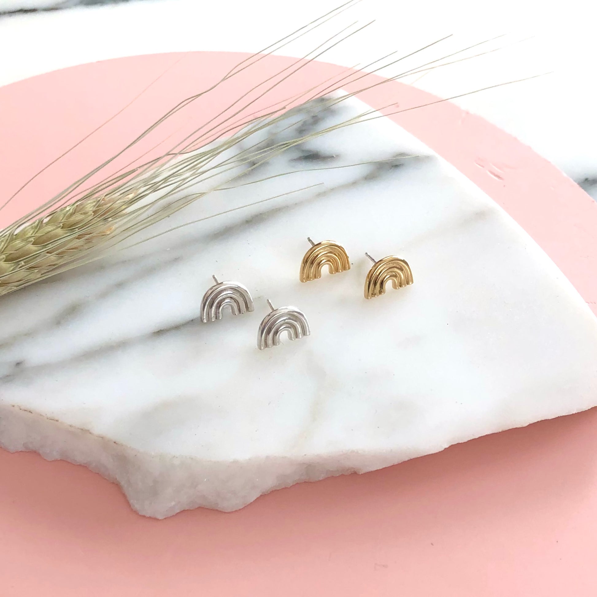 a pair of sterling silver and gold rainbow stud earrings displayed on a piece of marble with a pink background