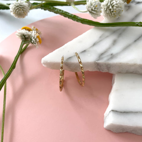Handmade gold hoop earrings on a marble displayed with a pink background and fresh flowers 