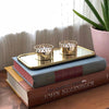 two brass tea light candle holders displayed on a mirror and two books. 