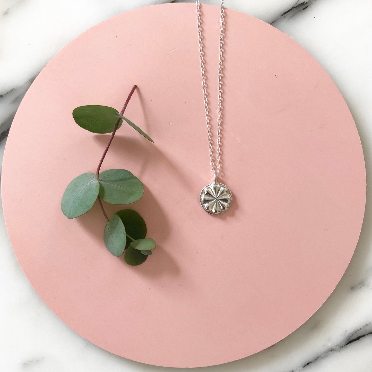 sterling silver circular medallion necklace on a gold chain with pink circular background with greenery