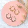 Geometric gold and silver hera hoops on a pink background and dried flowers