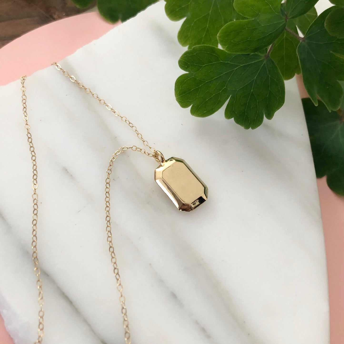 Gold Gemma Necklace displayed on a piece of marble with greenery