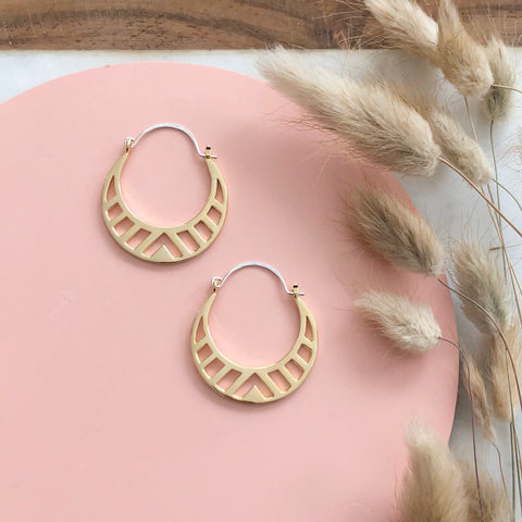 Gold hoop earrings with a cut geometric pattern on a pink background with dried flowers  