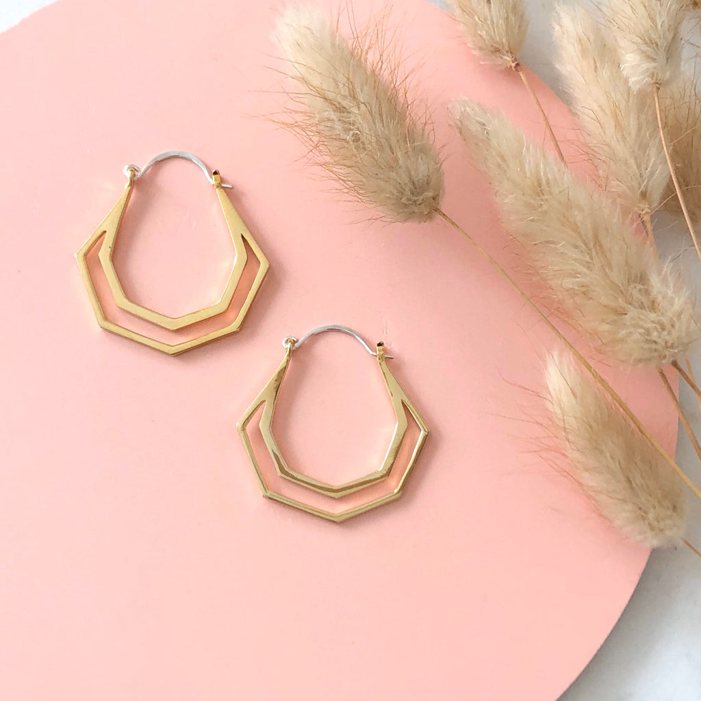 Geometric gold hera hoops on a pink background and dried flowers 