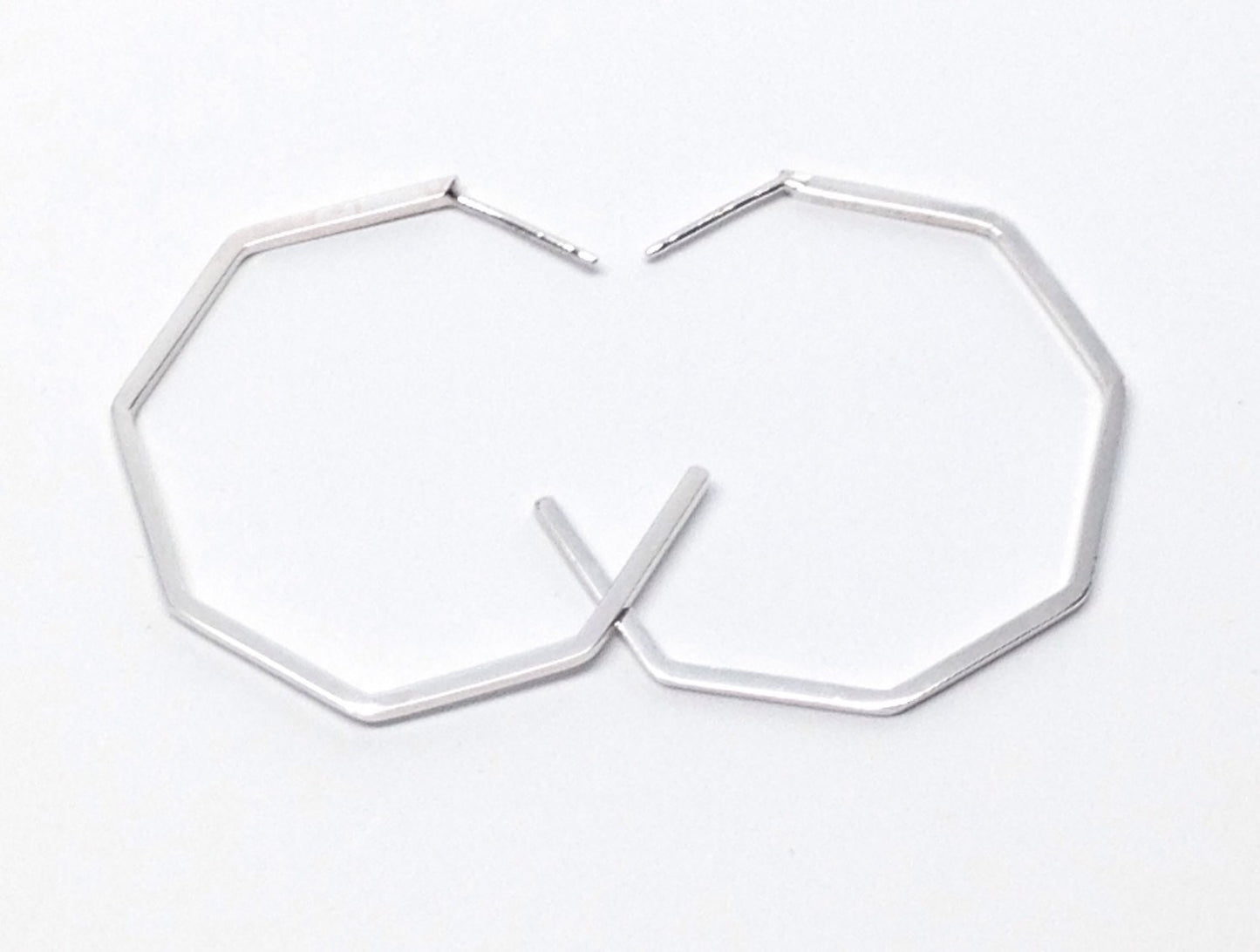 A pair of handmade sterling silver geometric hoop earrings on a white background