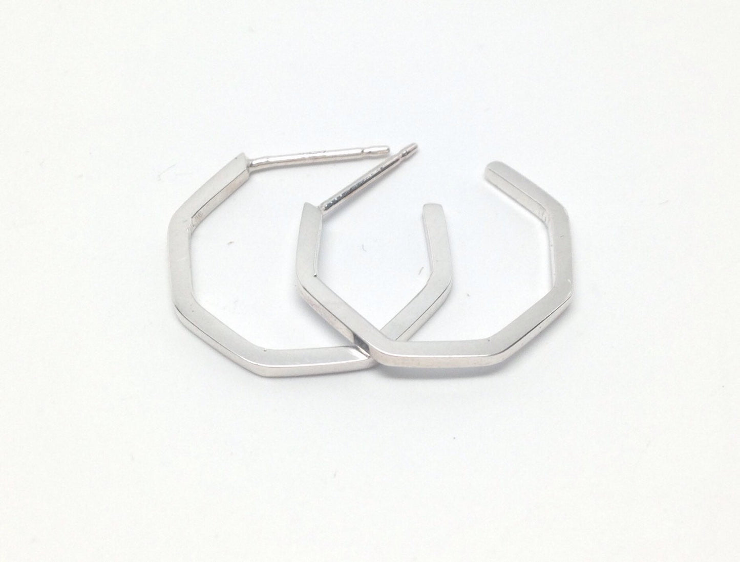 A pair of small sterling silver handmade geometric hoop earrings on a white background  